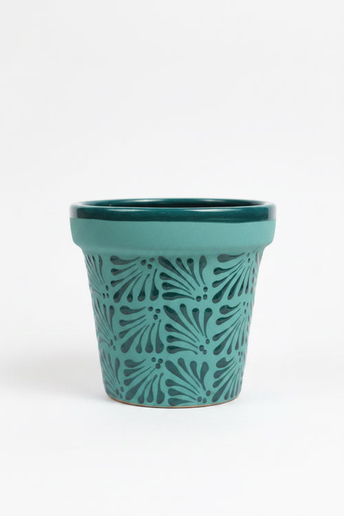 A turquoise ceramic planter pot with a dark teal leaf pattern.