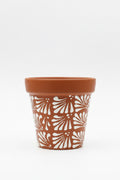 A terracotta-colored ceramic planter pot with a white hand-painted fan pattern.