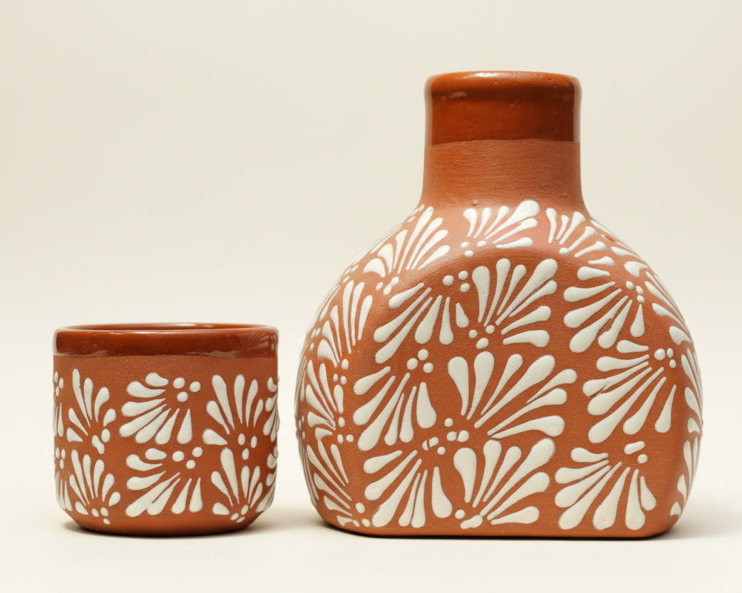 A terracotta-colored ceramic vase and matching small cup with a white raised floral pattern.