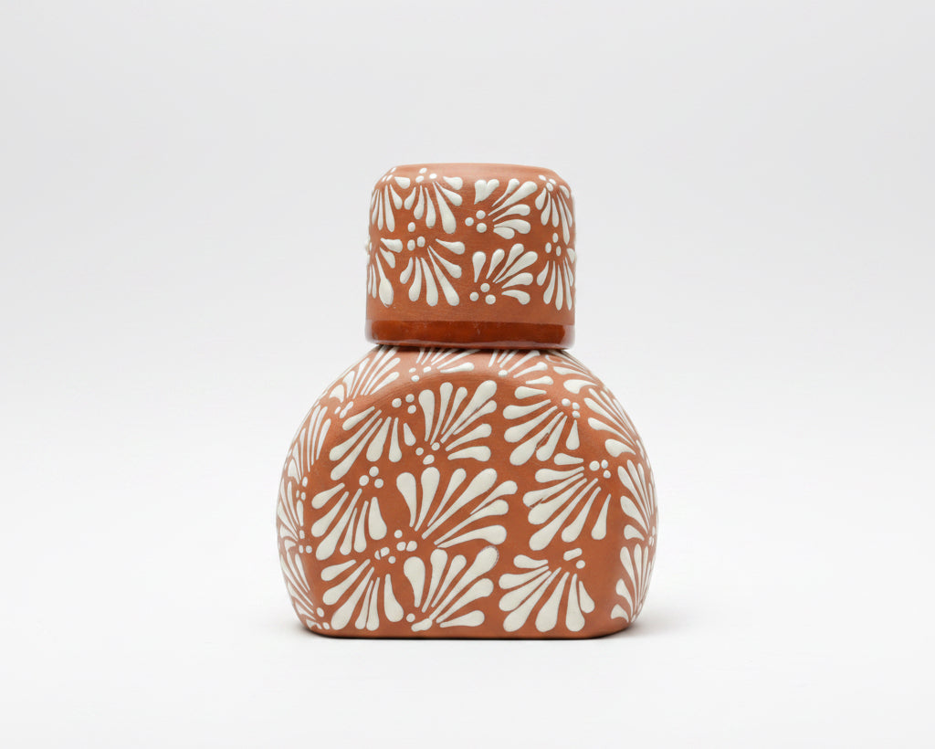 A terracotta-colored ceramic vase with a matching lid, featuring a raised white floral fan pattern.