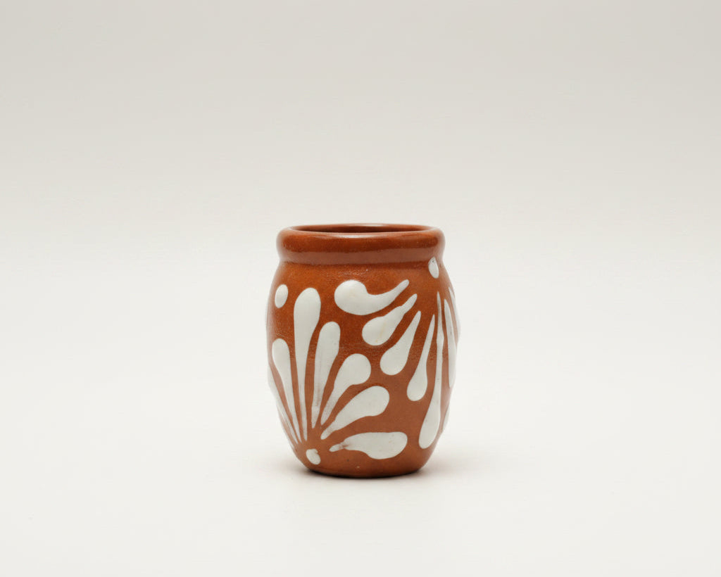 A small terracotta-colored ceramic pot with a white leaf pattern.