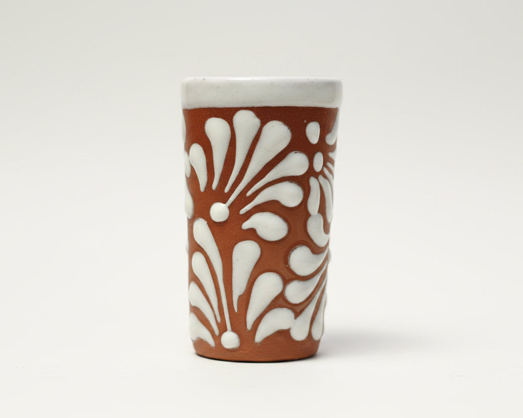 A terracotta-colored ceramic cup with a white raised floral pattern.